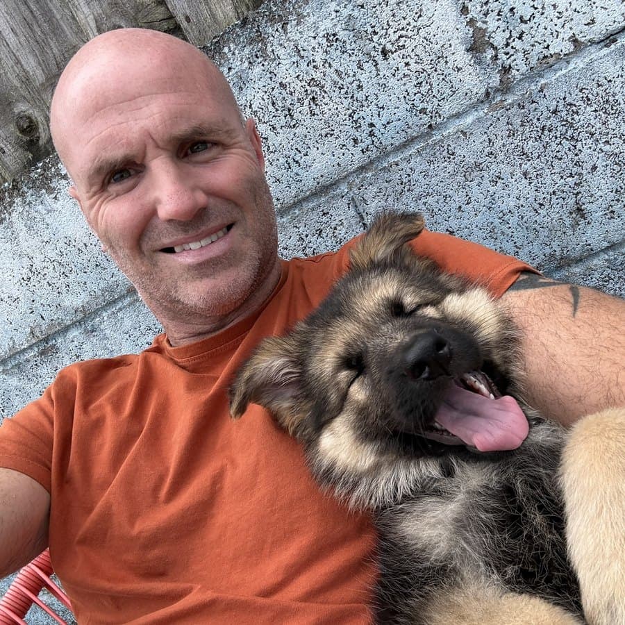 Steve Taylor, founder of TaskMyJob, sitting against a garden wall with his German Shepherd puppy.